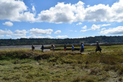 Students walk along the shoreline at Klingel-Bryan Beard Wildlife Refuge, under a bright blue sky with clouds.